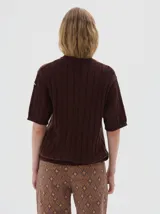 Remera de punto negra con cuello redondo y mangas cortas. Presenta un diseño de tejido con trenzas verticales.