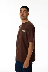 Remera marrón con estampa trasera de un pato con una ametralladora y un maletín lleno de dinero. En la parte superior de la estampa se lee "Vernal" en letras amarillas con estilo graffiti.