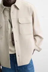 Sobrecamisa color beige de corte relaxed fit, con cuello solapa, manga larga con puños abotonados, bolsillos de plastrón con solapa en el pecho y bolsillos de vivo en la cadera. Cierre frontal con botones.