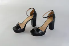 Sandalias negras de cuero con plataforma y tacón cuadrado. Tira delgada sobre los dedos y pulsera tobillera con hebilla dorada.