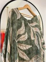 Blusa verde con estampado de hojas beige, cuello redondo y corte asimétrico.
