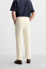 Pantalón color crudo de tejido con textura de rizo, corte relaxed fit, con cintura elástica, bolsillos frontales y traseros, cierre frontal con cremallera y botón.