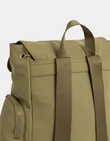 Mochila color beige con detalles en negro. Tiene solapa con tira de ajuste y broche, correas regulables, manija superior, bolsillo frontal con cierre y puller de cordón y goma, bolsillos laterales con cierres y pullers de cordón y goma, y tag de goma.