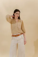 Blusa color beige con cuello mao con volantes, manga larga con puño elástico y cierre frontal con botones ocultos.
