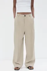Pantalón color beige de tiro medio con trabillas, pliegues frontales y corte ancho.