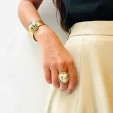 Anillo ajustable con una perla barroca irregular de color blanco nacarado, engarzada en una montura de metal dorado con textura.