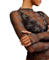 Top de manga larga, cuello alto y calce ajustado, confeccionado en tul negro transparente con estampado floral en gris. Presenta aberturas para los pulgares en los puños.