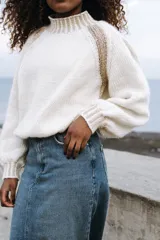 Sweater tejido a mano en lana merino y viscosa con lurex, color crudo con detalles dorados en cuello, puños y hombros. De corte holgado y cuello alto.