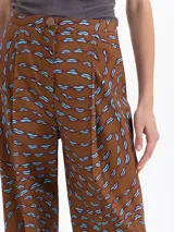 Pantalón de popelina con lycra color marrón, con estampado exclusivo de boquitas dinámicas en azul. Presenta pinzas en la cintura y el ruedo para un ajuste slim mom, cintura trasera elástica, bolsillos ojal en la espalda y bolsillos ocultos en los laterales. El acceso es mediante broche, cierre y botón interno a tono.