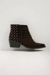 Bota corta de cuero color marrón oscuro (chocolate) con punta afilada y taco bajo. Presenta múltiples tiras decorativas con hebillas y tachas plateadas alrededor del empeine y el tobillo, además de tachas en el borde de la suela.