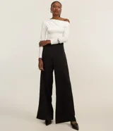 Blusa corta color blanco, con escote canoa que deja un hombro al descubierto y mangas largas.