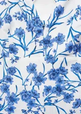 Mono largo blanco con estampado floral azul, escote de pico y tirantes finos cruzados en la espalda.