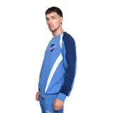 Buzo deportivo Umbro del Club Nacional de Football, color rojo con mangas azul marino y detalles blancos en hombros y laterales. Presenta el logo de Umbro bordado en el pecho y el escudo del club en el lado derecho.