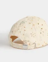Gorra de béisbol color crema con bordado calado y estampado de flores en tonos pastel. Cuenta con visera curva y tira ajustable en la parte trasera.