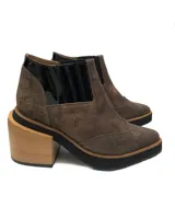 Botinetas de cuero vacuno color marrón con elásticos laterales negros, detalle de charol negro en el talón y puntera con diseño brogue. Taco de madera de 5 cm y plataforma de 2 cm. Suela de goma antideslizante.