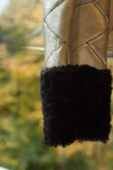 Chaqueta de cuero plateada con acabado metalizado y diseño acolchado. Presenta cuello y puños de piel en color negro, cierre frontal metálico y bolsillos laterales con cremallera.