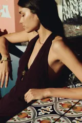 Vestido largo marrón de punto pointelle con estilo crochet, corte entallado, escote halter en V, adorno de metal en forma de sol en el centro del busto y falda sirena con bajo recto.