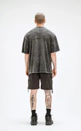 Remera de cuello redondo, calce oversize, color gris oscuro con efecto batik artesanal (acid wash). Presenta un corte curvo en la parte superior del pecho que simula un recorte.