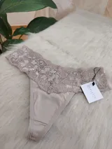 Bombacha tipo tanga color beige con encaje floral en la parte superior.