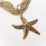 Collar dorado con múltiples hilos de cuentas pequeñas y dije grande de estrella de mar texturizada.
