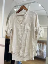 Camisa celeste de lino, con cuello mao, manga 3/4 con botón para sujetar, cierre frontal con botones y bolsillo de parche en el pecho.