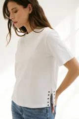 Remera blanca de algodón de corte recto, con cuello redondo y mangas cortas. Presenta detalle de aberturas laterales con ojales metálicos.