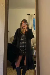 Vestido corto de cuero negro, con escote recto y tirantes finos. El cuerpo del vestido está adornado con múltiples hebillas metálicas plateadas dispuestas en filas verticales.