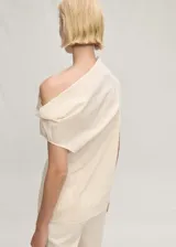 Blusa color crema sin mangas, con cuello asimétrico drapeado y corte recto.