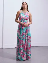 Vestido largo de gasa estampada con flores rosas y turquesas sobre fondo blanco. Tiene escote halter con ojal, cintura fruncida y falda con sobrecapa.