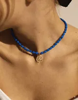 Gargantilla corta con cuentas de cristal azul y dije circular dorado con diseño calado.