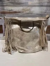 Cartera plateada con textura brillante y flecos laterales. Tiene un asa circular metálica y correa larga desmontable.
