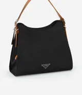 Cartera hobo grande color negro con asa mediana contrastante color marrón y detalle triangular de metal con el logo de la marca.