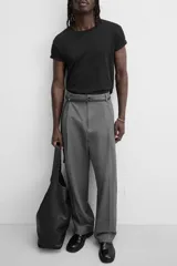 Pantalón gris de corte ancho con pliegues frontales y cinturón fino negro.