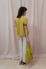 Blusa blanca de lino con escote en V, mangas cortas abullonadas y cierre frontal con lazos.