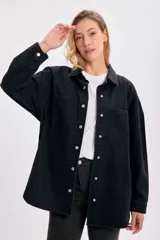 Sobrecamisa de jean negro con cuello clásico, cierre frontal con botones a presión, dos bolsillos con solapa en el pecho y corte holgado.