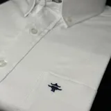 Camisa blanca de algodón oxford con spandex, de manga larga, cuello abotonado y bolsillo en el pecho con logo bordado.