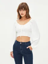 Blusa corta blanca con escote cuadrado, mangas largas abullonadas y lazo ajustable en el centro del busto.