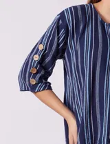 Blusa de algodón con estampado a rayas verticales en tonos celeste, rosa y blanco. Tiene cuello redondo con escote en V y abertura con botones de madera. Las mangas son 3/4 con aplique de botones.