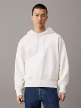 Buzo con capucha confeccionado en felpa de algodón regenerativo color blanco. Tiene corte relaxed, capucha con cordón, puños y bajo de canalé, logo bordado en el bajo en el mismo tono y estampado fotográfico digital de Calvin Klein en la parte trasera.