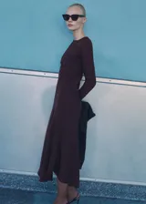 Vestido midi marrón oscuro de tejido ligero con cuello redondo y manga larga. Presenta un diseño evasé con detalle drapeado en la cintura y cierre de cremallera en la parte posterior.