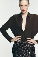 Camisa marrón de seda 100% con cuello solapa, manga larga con puños abotonados, bajo asimétrico redondeado y cierre frontal con botones.
