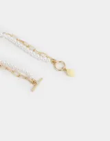 Set de dos pulseras: una con perlas blancas y otra con cadena dorada de eslabones grandes. Cierre con barra en forma de T y dije colgante en forma de lágrima color amarillo pastel.