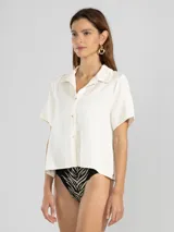 Camisa de manga corta color blanco hueso confeccionada en una mezcla de lino, lyocell y viscosa. Tiene cuello camisero y cierre abotonado al frente.