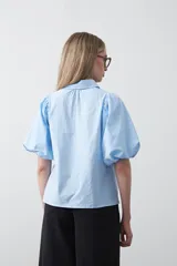 Camisa blanca de algodón con cuello camisero y mangas cortas abullonadas. Presenta un corte relajado y cierre frontal de botones.