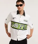 Camisa blanca oversized de tricolina con cuello negro contrastante, mangas cortas y estampado con la palabra "Hustle" en verde y negro.