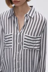 Camisa a rayas verticales grises y blancas, con cuello camisero, cierre frontal con botones, mangas largas con trabillas para enrollar y dos bolsillos de parche en el pecho.