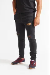 Jean skinny de hombre color negro, ajustado desde la cadera hasta los tobillos, con roturas en las rodillas y logo bordado en el bolsillo trasero.