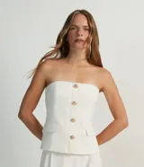 Blusa estilo corset color blanco, con escote recto, sin mangas, abotonado frontal y solapas aplicadas.