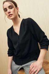 Camisa marrón de manga larga con escote en V y botones forrados al tono en el frente. Destaca por su textura sutil y por el detalle de frunces con volados en la parte inferior.