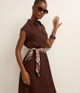 Vestido chemise de lino color negro, con cuello camisero, sin mangas y cierre frontal con botones. Incluye cinturón de tela estampado.